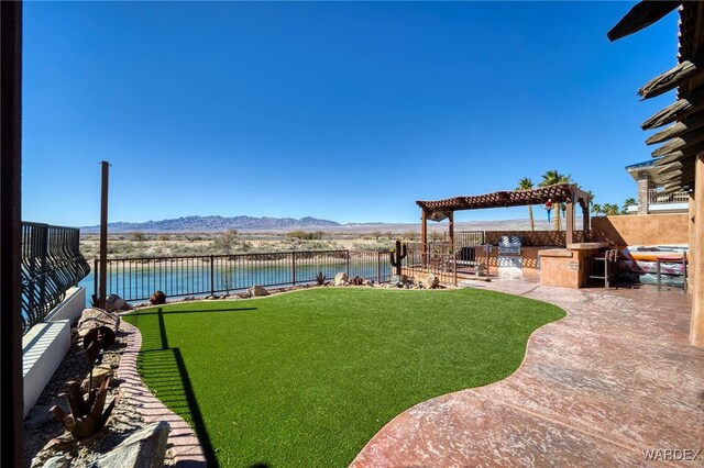 view of yard featuring a patio, an outdoor kitchen, a fenced backyard, a water and mountain view, and a pergola