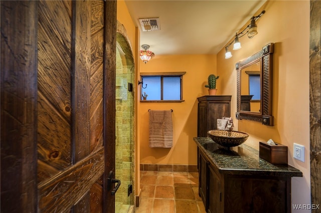 bathroom featuring visible vents, stone finish floor, vanity, a shower stall, and baseboards