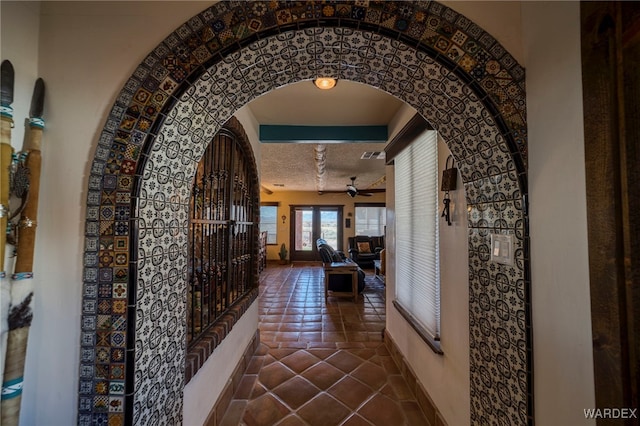 hall with baseboards, tile patterned flooring, arched walkways, and a textured ceiling