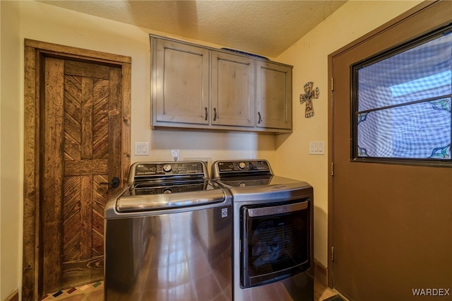 clothes washing area with a textured ceiling, washer and clothes dryer, and cabinet space