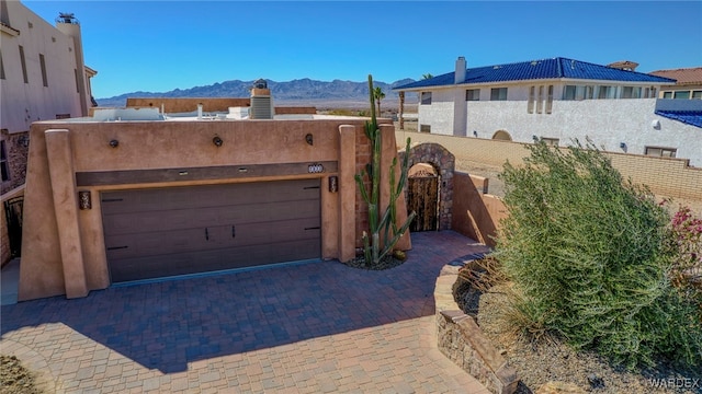 view of front of property featuring a mountain view, a garage, fence, decorative driveway, and stucco siding