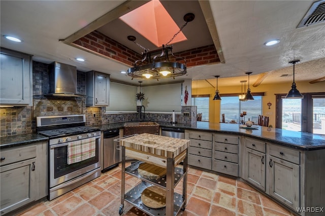 kitchen with stainless steel appliances, visible vents, a sink, wall chimney range hood, and a peninsula