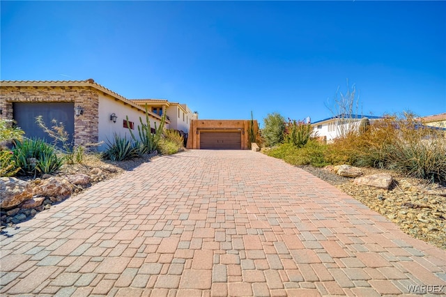 view of front of home featuring decorative driveway, stone siding, a garage, and stucco siding