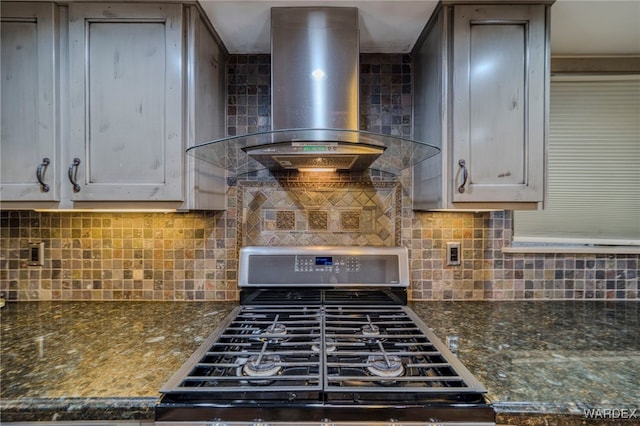 kitchen with dark stone countertops, wall chimney range hood, decorative backsplash, and gas range oven