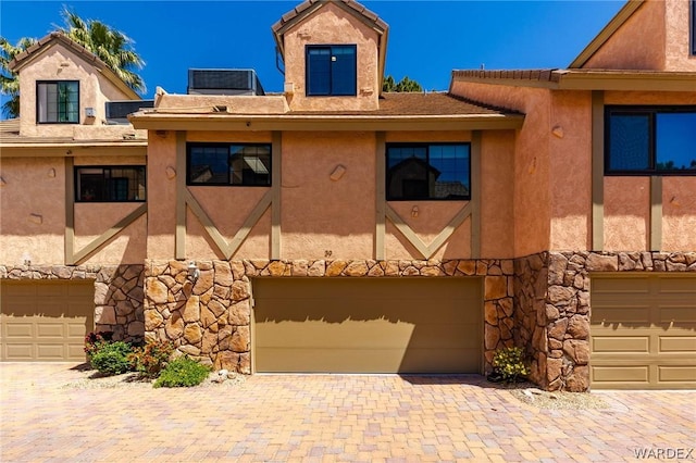 view of front facade featuring stone siding, an attached garage, and stucco siding