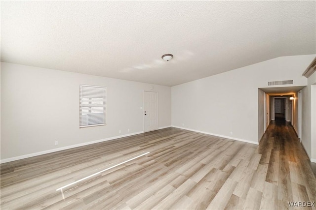 spare room featuring lofted ceiling, light wood-style floors, visible vents, and a textured ceiling