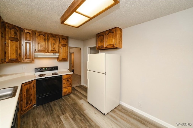 kitchen with under cabinet range hood, brown cabinets, range with electric stovetop, freestanding refrigerator, and wood finished floors