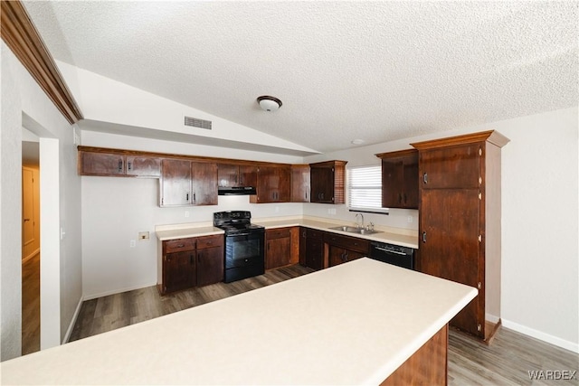 kitchen featuring black appliances, under cabinet range hood, a sink, light countertops, and vaulted ceiling