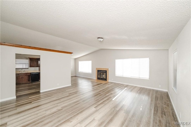 unfurnished living room with light wood finished floors, a tile fireplace, baseboards, and lofted ceiling