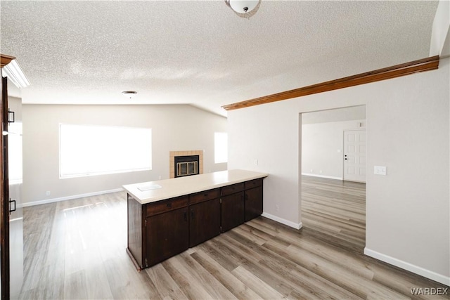 kitchen with dark brown cabinets, a tiled fireplace, light countertops, a peninsula, and light wood-style floors