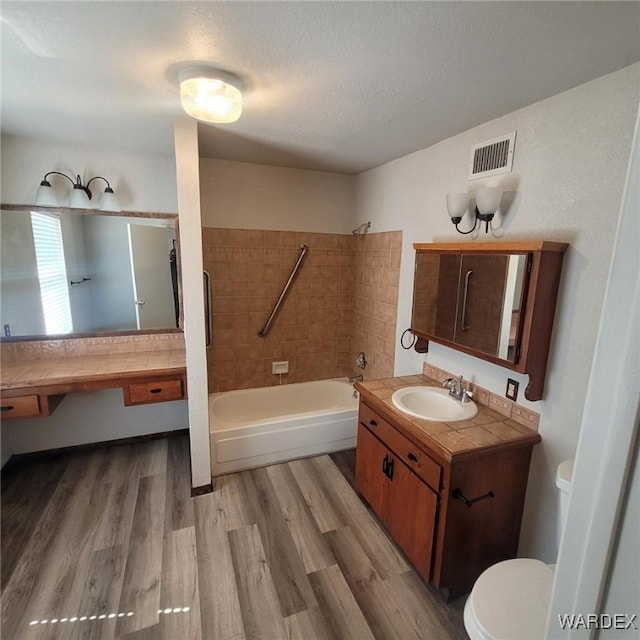 full bath featuring visible vents, toilet, bathing tub / shower combination, wood finished floors, and a textured ceiling