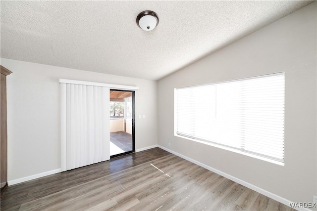 unfurnished bedroom with lofted ceiling, wood finished floors, baseboards, and a textured ceiling