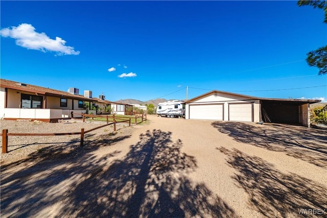 exterior space featuring dirt driveway, a detached garage, an outdoor structure, and fence