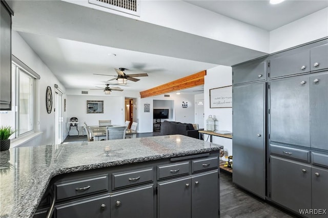 kitchen with visible vents, a ceiling fan, stone countertops, dark wood-style floors, and a peninsula