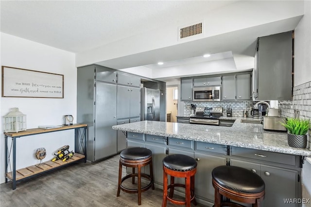 kitchen featuring visible vents, a peninsula, a sink, gray cabinetry, and appliances with stainless steel finishes