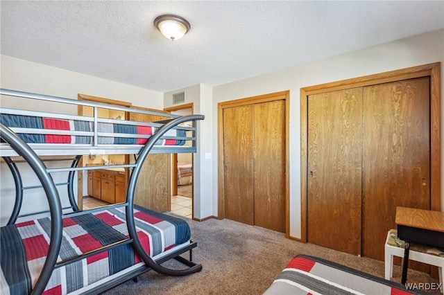 carpeted bedroom with visible vents, a textured ceiling, and two closets