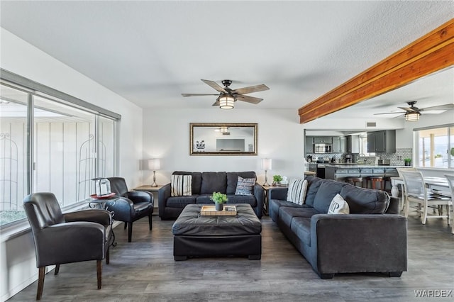 living area featuring beam ceiling, wood finished floors, and a ceiling fan