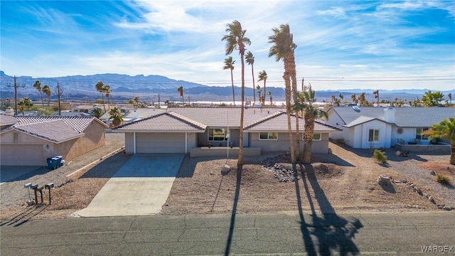 single story home featuring stucco siding, concrete driveway, a garage, a tiled roof, and a mountain view