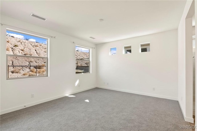 empty room with carpet, visible vents, and baseboards