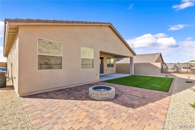 rear view of property featuring stucco siding, a patio, a fire pit, and fence