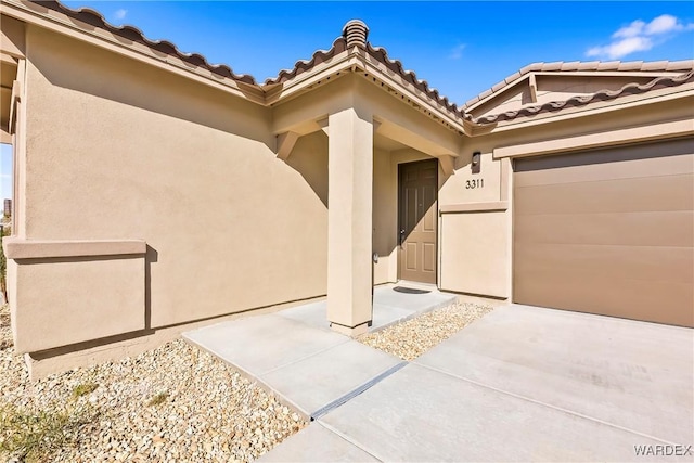 doorway to property with a garage, a tiled roof, and stucco siding