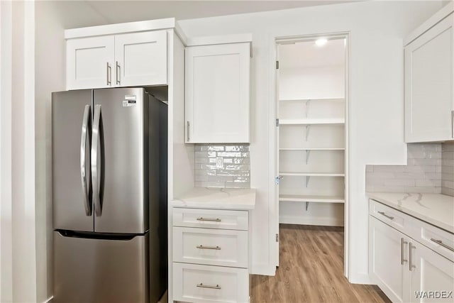 kitchen featuring light stone counters, white cabinetry, freestanding refrigerator, decorative backsplash, and light wood finished floors