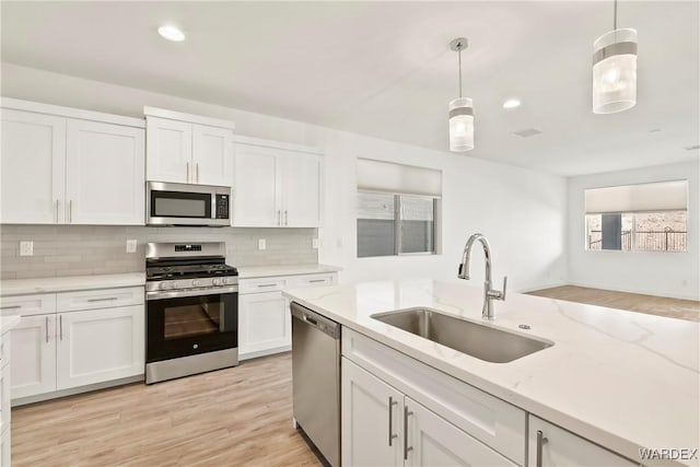 kitchen featuring white cabinets, decorative light fixtures, light stone countertops, stainless steel appliances, and a sink