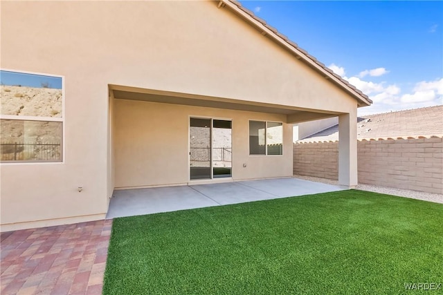 rear view of property featuring a patio, a tile roof, fence, a yard, and stucco siding