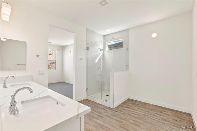 bathroom with a stall shower, wood finished floors, a sink, and double vanity