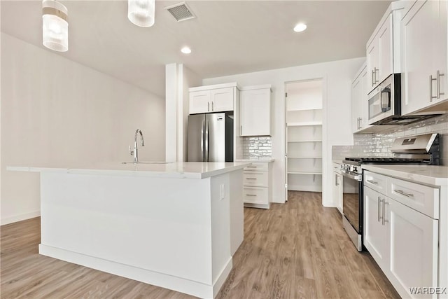 kitchen featuring white cabinets, light countertops, appliances with stainless steel finishes, an island with sink, and pendant lighting