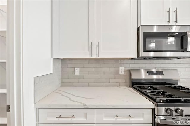 kitchen featuring light stone countertops, white cabinetry, stainless steel appliances, and decorative backsplash