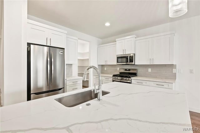 kitchen with decorative light fixtures, appliances with stainless steel finishes, white cabinetry, a sink, and light stone countertops