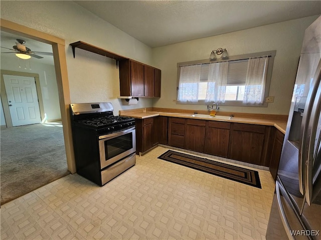 kitchen with dark brown cabinetry, light carpet, a sink, light countertops, and appliances with stainless steel finishes