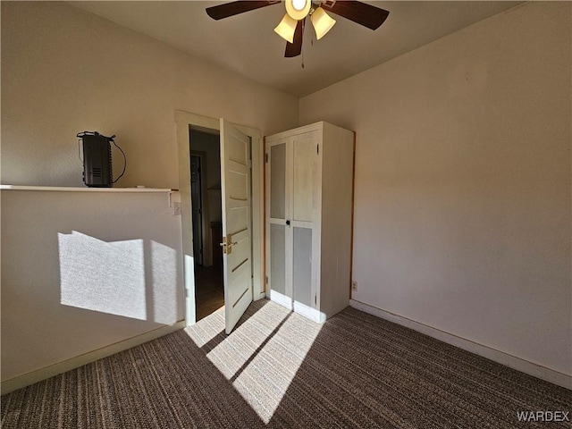 interior space featuring a ceiling fan, dark colored carpet, and baseboards