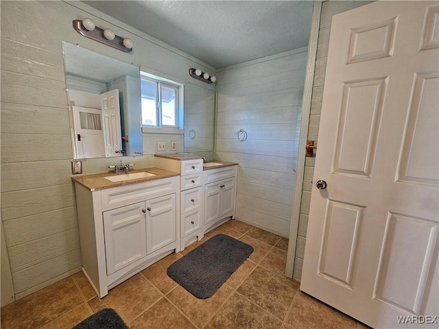 bathroom featuring double vanity, a sink, wooden walls, a textured ceiling, and tile patterned flooring