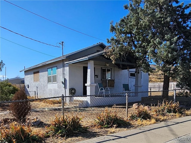 bungalow with a fenced front yard, covered porch, and stucco siding