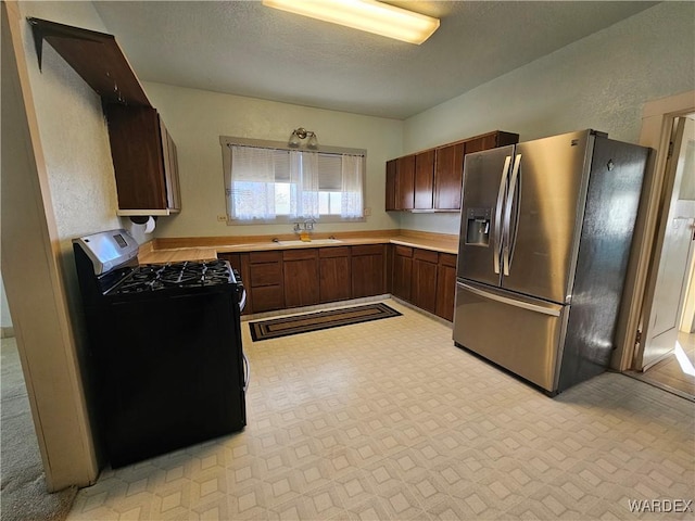 kitchen featuring light countertops, gas stove, a sink, a textured ceiling, and stainless steel fridge with ice dispenser