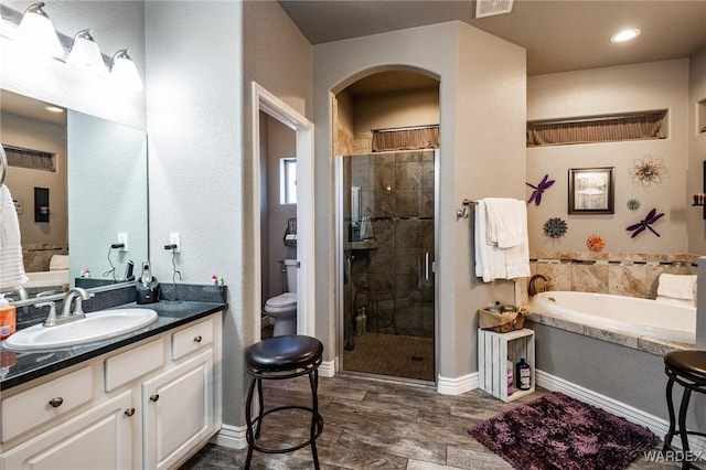 full bathroom featuring toilet, a stall shower, a garden tub, and vanity