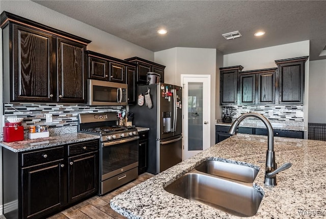 kitchen with light stone counters, light wood-style flooring, a sink, appliances with stainless steel finishes, and decorative backsplash