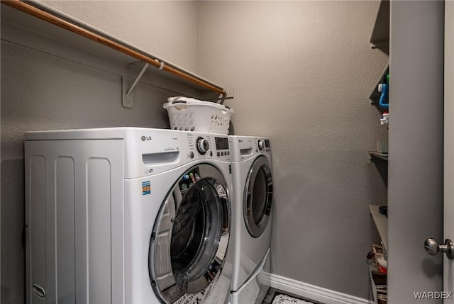 clothes washing area featuring a textured wall, laundry area, washer and clothes dryer, and baseboards