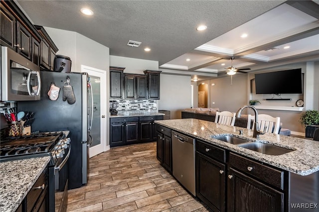 kitchen with a sink, appliances with stainless steel finishes, backsplash, wood tiled floor, and an island with sink