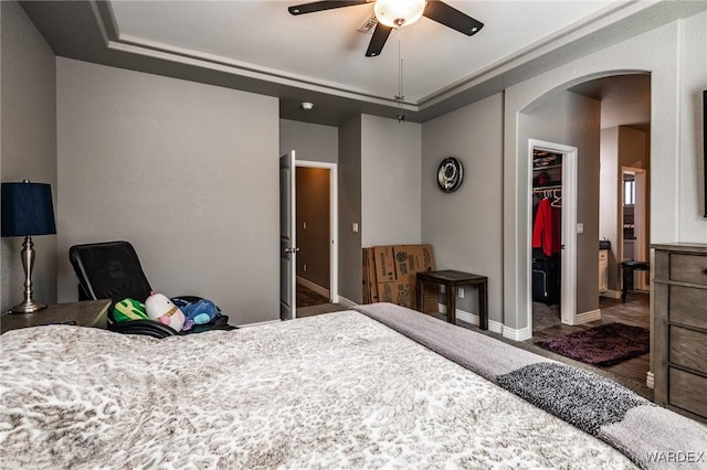 bedroom with arched walkways, a ceiling fan, baseboards, a closet, and a walk in closet