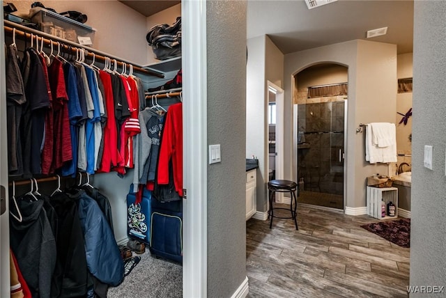 walk in closet featuring arched walkways, wood finished floors, and visible vents