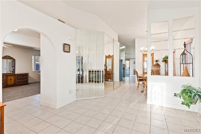 empty room featuring light tile patterned floors, baseboards, arched walkways, light colored carpet, and an inviting chandelier