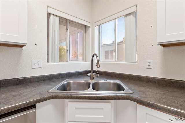 kitchen featuring dishwasher, dark countertops, a sink, and white cabinetry