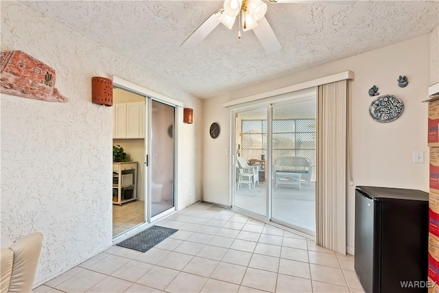 doorway featuring ceiling fan, a textured ceiling, and light tile patterned floors