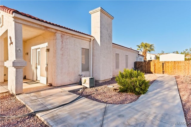 view of side of home with a tile roof, fence, a chimney, and stucco siding