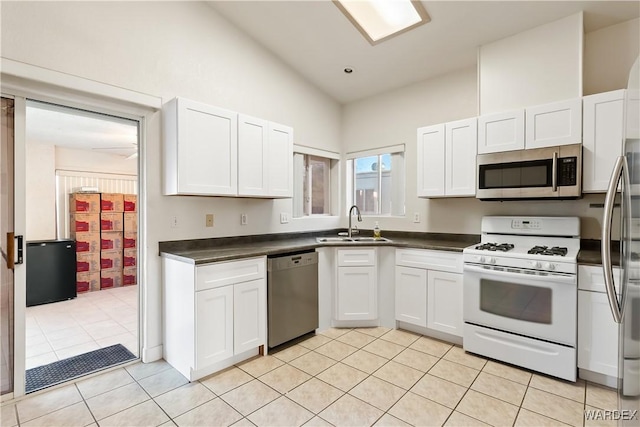 kitchen featuring stainless steel appliances, dark countertops, white cabinets, and a sink