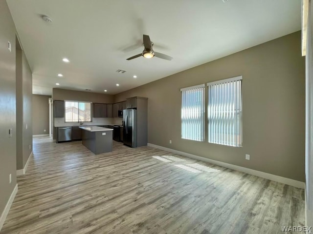 kitchen with stainless steel appliances, a kitchen island, light wood-style floors, open floor plan, and light countertops