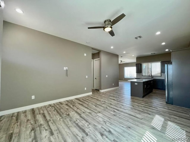 kitchen with a kitchen island, baseboards, open floor plan, light countertops, and freestanding refrigerator